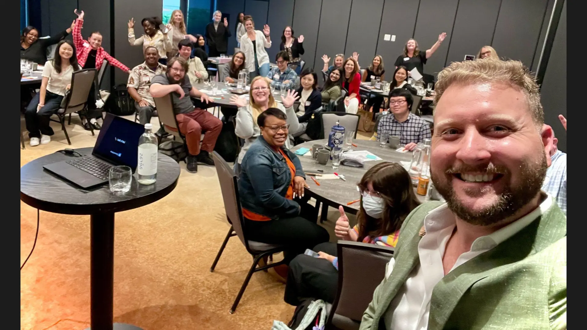 A full room of attendees waving during a Corey Peck live training